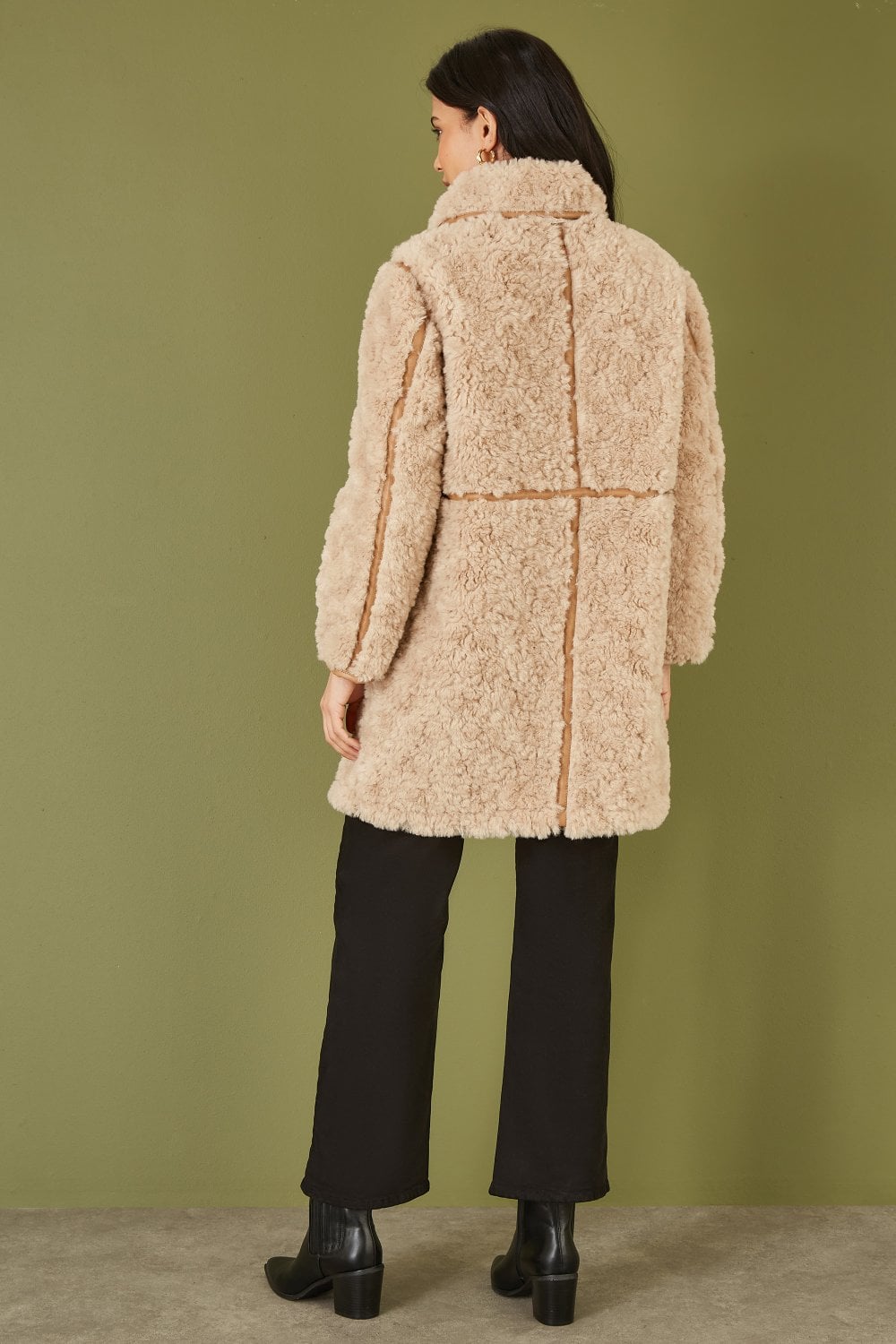 Person wearing a beige teddy coat against a green background