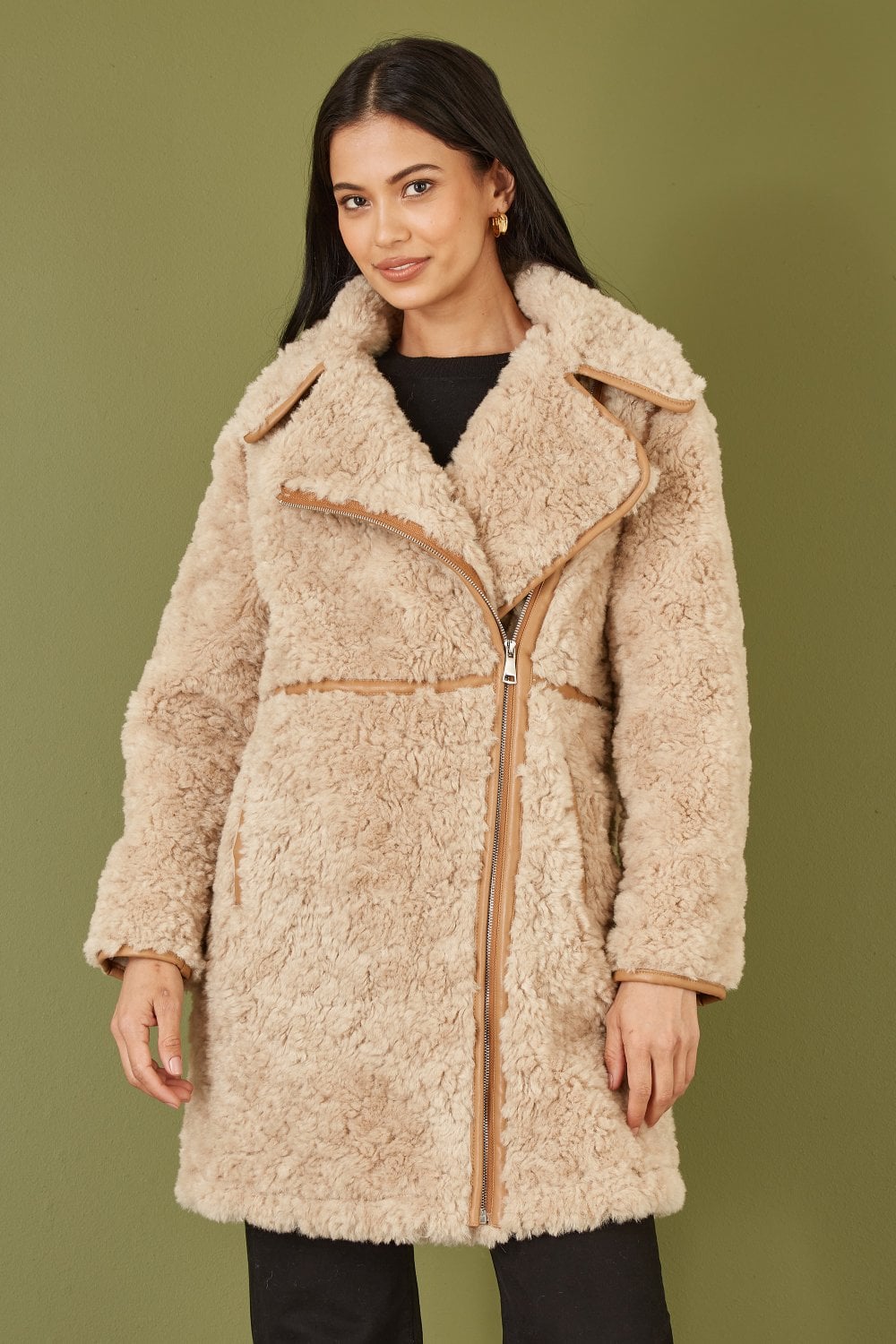 Woman wearing a beige sherpa coat against a green background