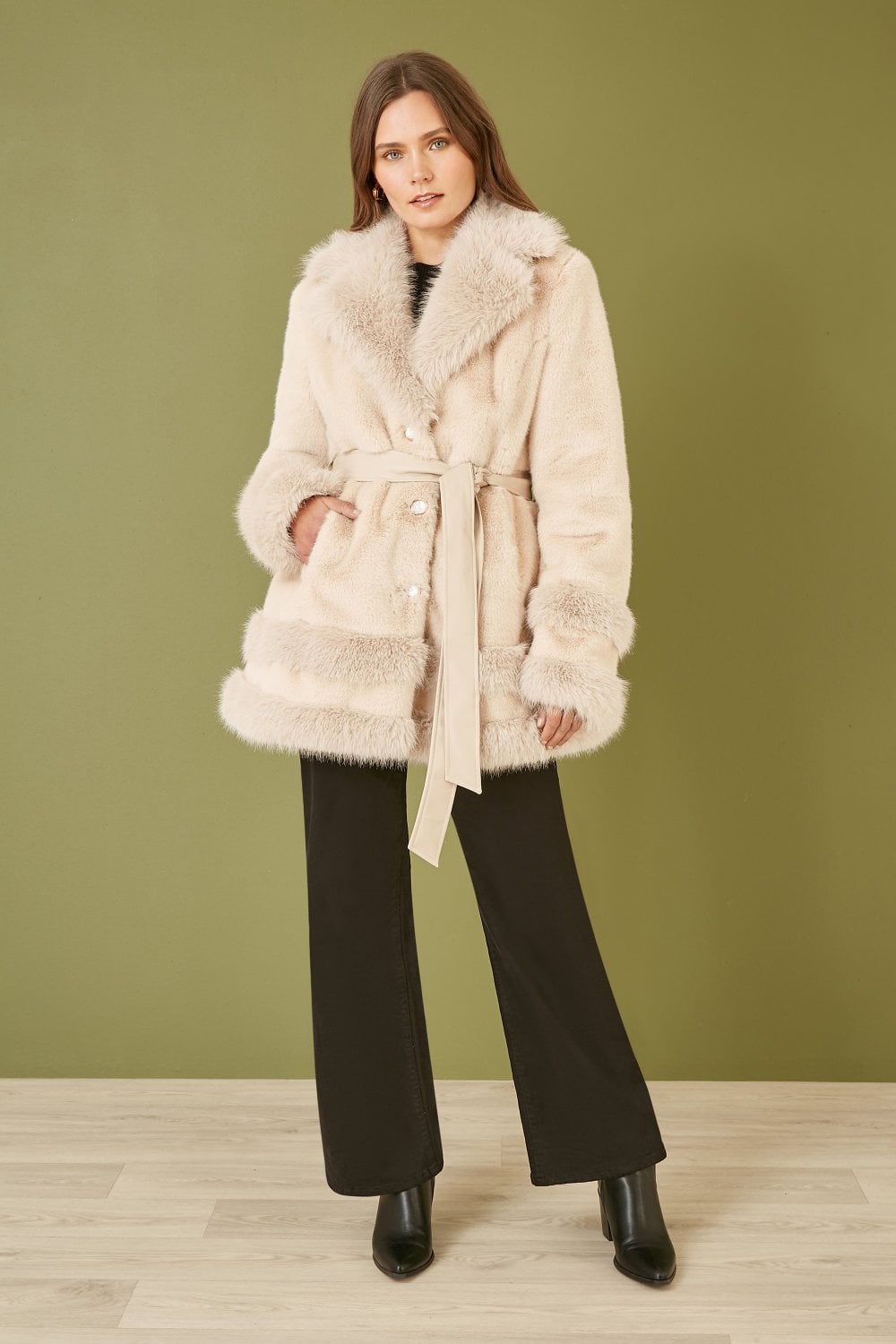 Woman wearing a cream fur coat against a green wall