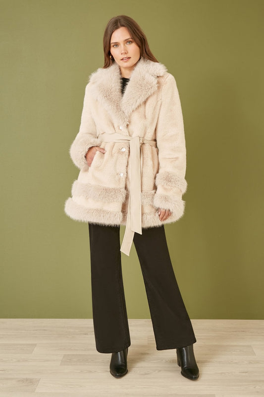 Woman wearing a cream fur coat against a green wall
