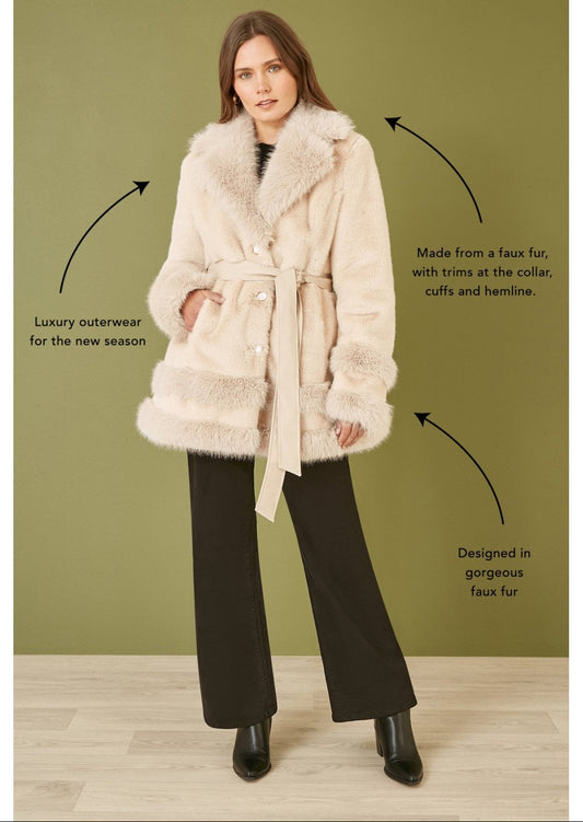 Woman wearing a cream faux fur swing coat with text describing the product on a green background