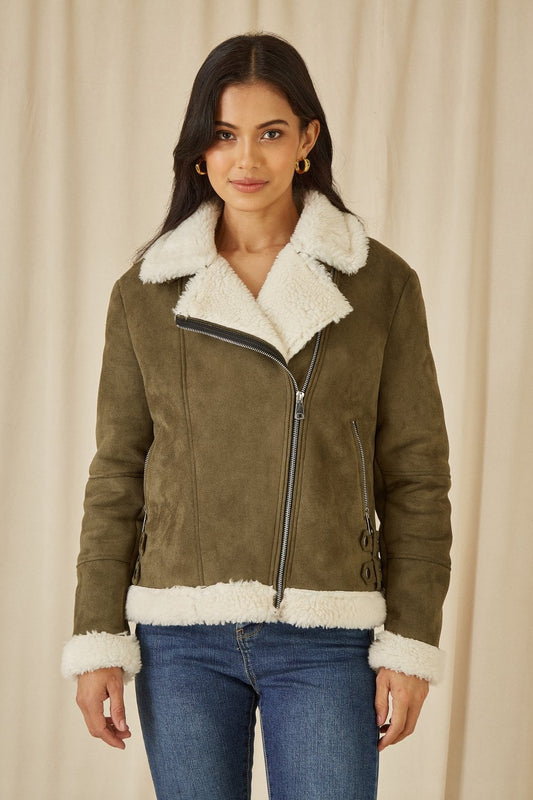 Woman wearing a green suede jacket with white fur trim against a beige background
