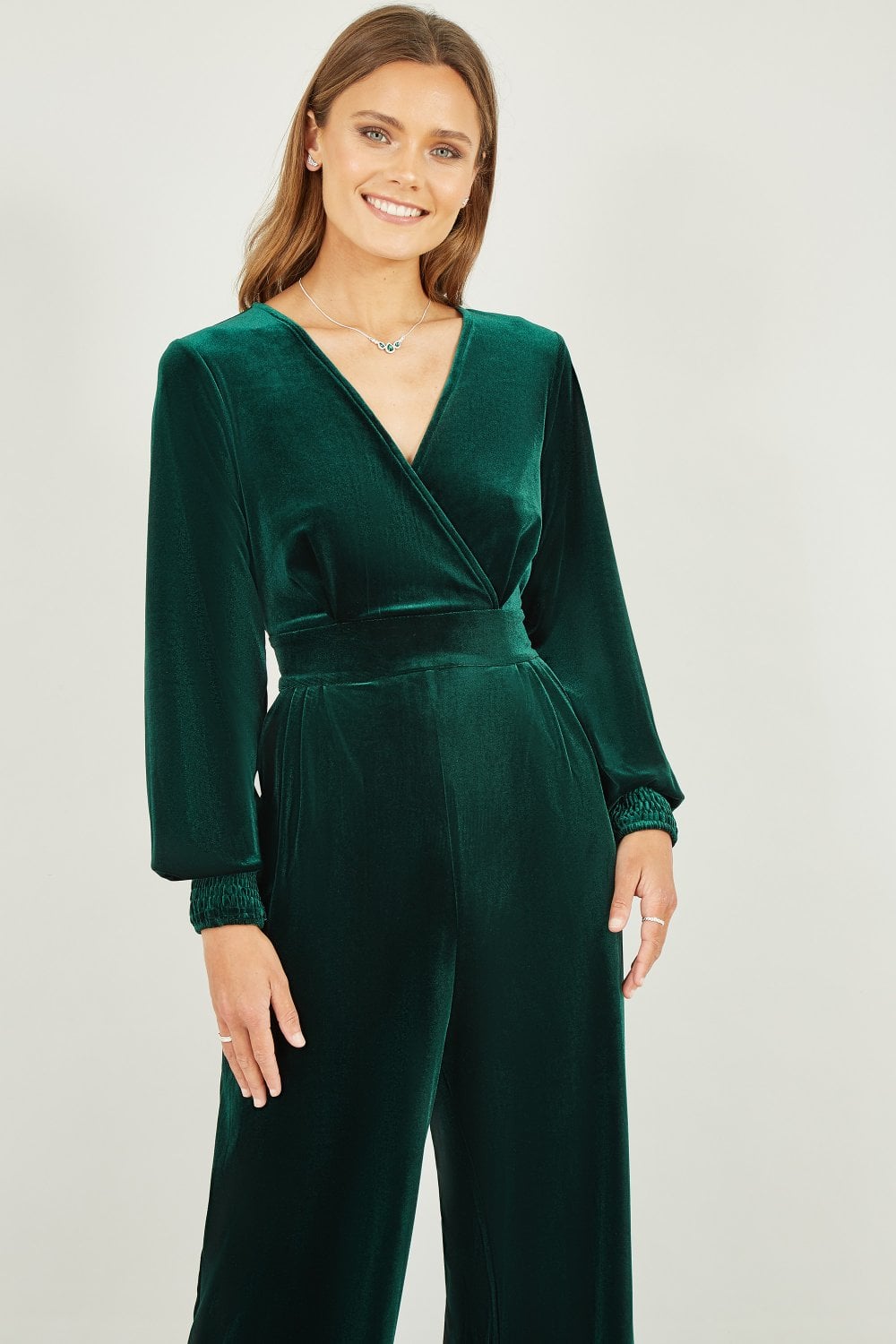 Woman wearing a green velvet jumpsuit on a plain background