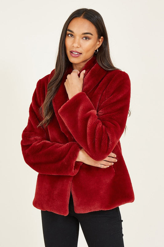 Woman wearing a red faux fur coat against a plain background