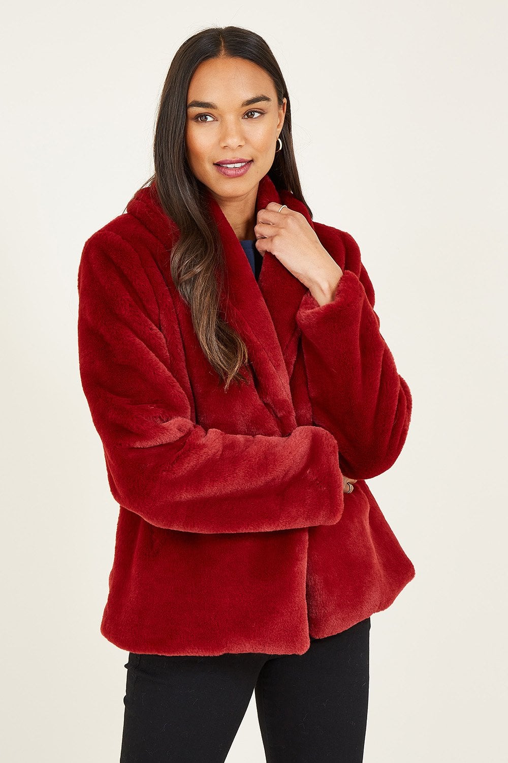 Woman wearing a red plush coat against a beige background