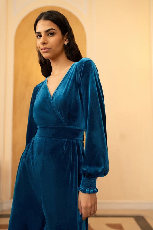 Woman wearing a blue velvet dress standing against a beige wall.