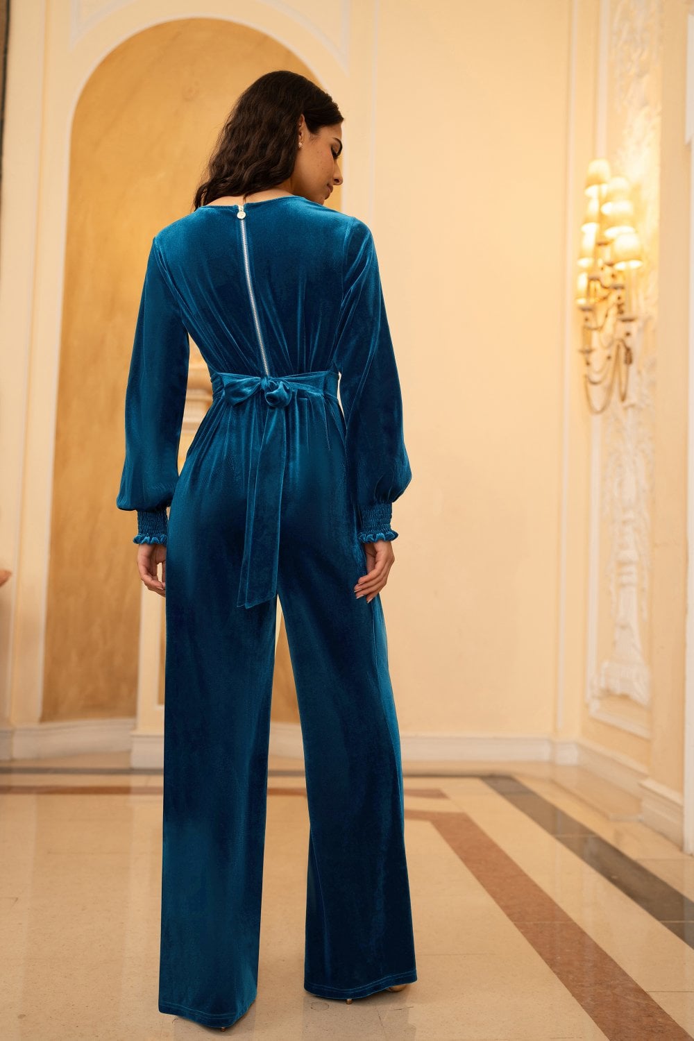 Woman wearing a blue velvet jumpsuit in an elegant interior setting